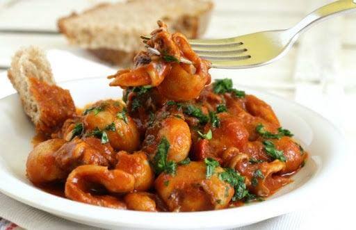 Plate of seppie al pomodoro with fresh herbs and bread, showcasing a delicious seafood dish.