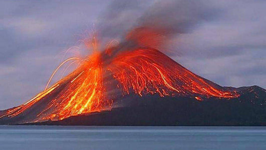 Erupting Stromboli volcano with lava flow and smoke against a twilight sky.