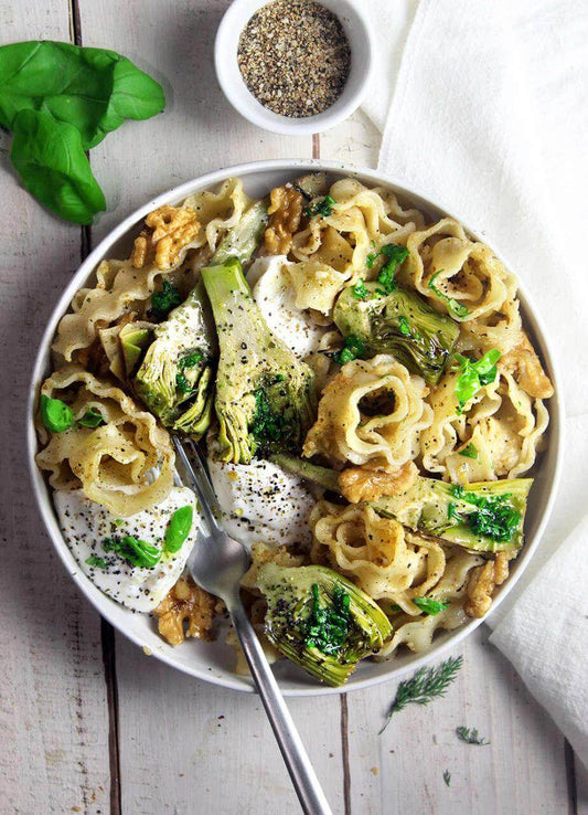 Vermicelli pasta with artichokes, topped with herbs and spices, served in a white bowl.