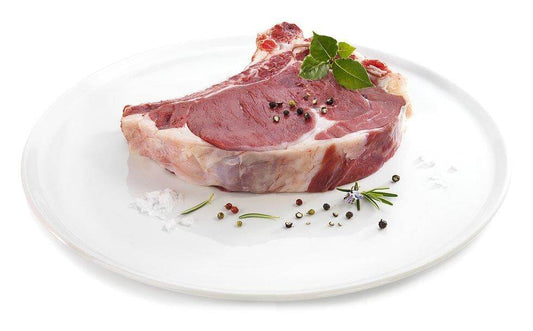 Raw beef rib steak with herbs and spices on a white plate, ready for grilling.
