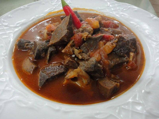 Succulent soffritto di maiale in un piatto bianco, con pezzi di carne, pomodori e peperoncino rosso.
