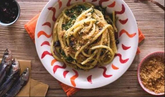 Pasta with sardines, Italian seasonal dish, served in a decorative bowl with fresh herbs and breadcrumbs.