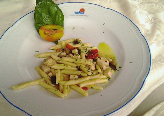 Plate of Strangugghia Previti pasta with vegetables and herbs, garnished with fresh basil and tomato.