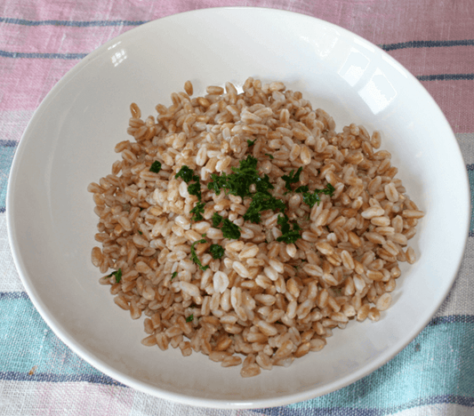 Bowl of cooked grains garnished with fresh parsley on a colorful tablecloth.