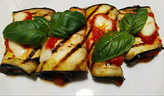 Involtini di melanzane con mozzarella e salsa di pomodoro, guarniti con foglie di basilico fresco.