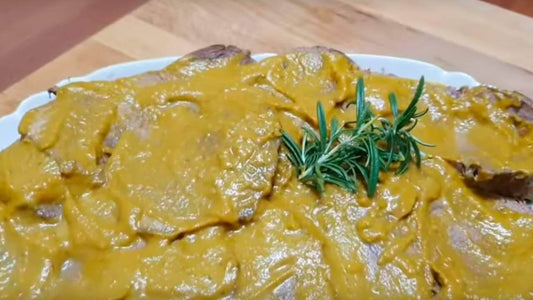 Sliced noce di vitello in a creamy sauce, garnished with fresh rosemary on a wooden table.