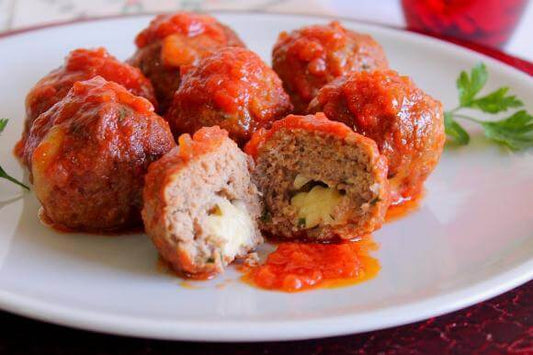 Delicious meatballs in tomato sauce, featuring melted cheese inside, served on a white plate.