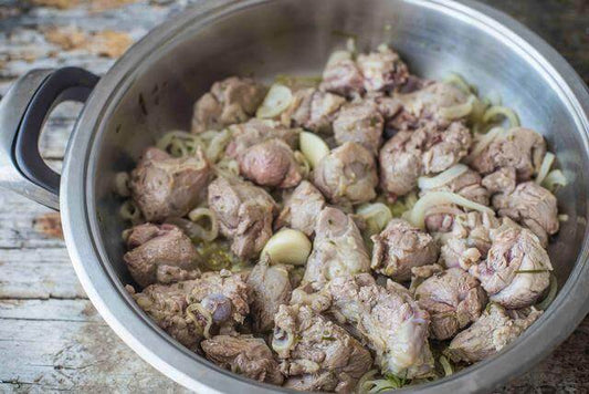 Tender pieces of capretto meat cooking with onions in a stainless steel pot.