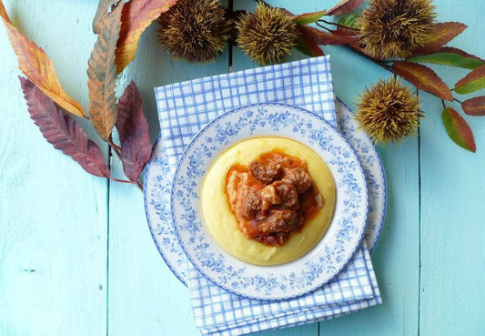 Plate of polenta topped with rich meat sauce, surrounded by autumn leaves on a blue wooden table.