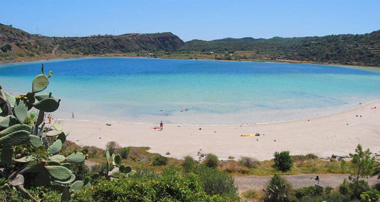 Scenic view of Pantelleria's crystal-clear lagoon with sandy beach and lush vegetation.