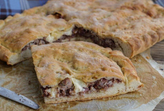 Slice of Sicilian focaccia filled with sausage and caciocavallo cheese on a wooden board.