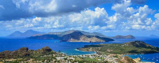 Panoramic view of the Eolie Islands, featuring lush landscapes and blue waters under a cloudy sky.