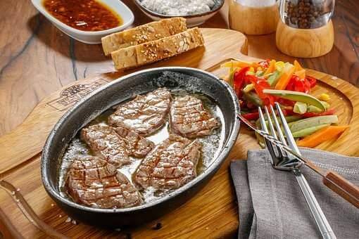 Delicious grilled meat served in a sizzling platter with colorful vegetables and bread on a wooden table.