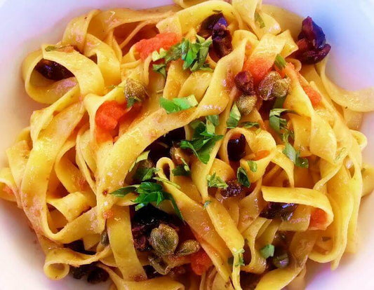 Tagliatelle Contadine topped with herbs and dried fruits in a white bowl.