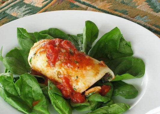 Involtini di tonno su un letto di spinaci freschi, con salsa di pomodoro e formaggio, serviti in un piatto bianco.