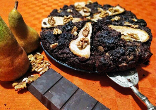 Delicious chocolate, pear, and walnut cake garnished with pear slices and walnuts on an orange background.