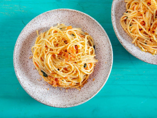 Plate of spaghetti alla Carrettiera topped with breadcrumbs on a vibrant turquoise table.