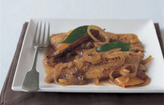 Plate of fried sole with caramelized onions, cinnamon, and bay leaves, garnished elegantly.