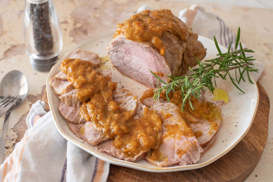 Succulent roasted veal served with rich sauce, garnished with rosemary on a rustic wooden platter.