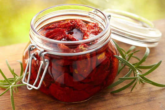 Jar of sun-dried tomatoes in olive oil with rosemary on a wooden surface.