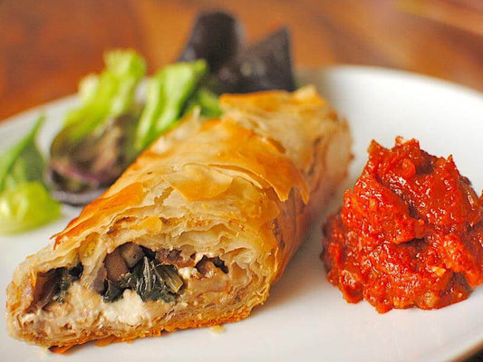 Delicious meat strudel served with fresh salad and spicy tomato sauce on a white plate.