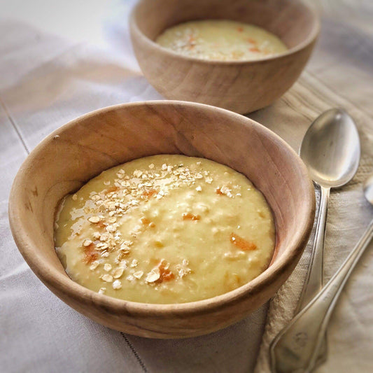 Creamy oat soup topped with oat flakes served in wooden bowls with spoons on a linen tablecloth.