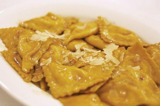 Plate of agnolotti pasta topped with shaved cheese, showcasing traditional Italian cuisine.