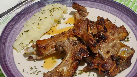 Grilled lamb chops served with creamy mashed potatoes and garnished with herbs on a purple plate.
