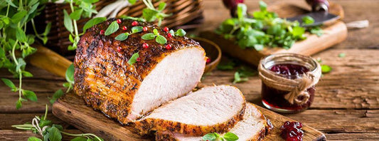 Deliciously roasted pork with herbs and garnishes served on a wooden board.