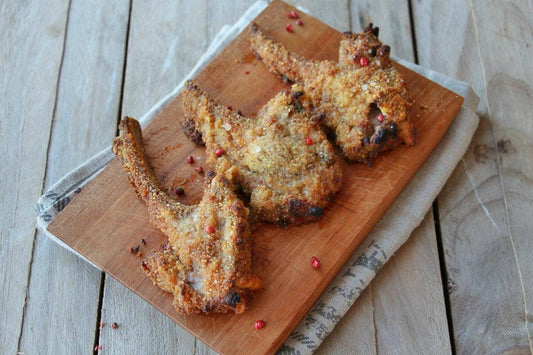 Crunchy lamb chops on a wooden cutting board, garnished with pink peppercorns.