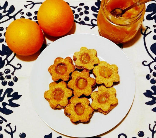 Delicious Occhi di Bue cookies on a plate, surrounded by fresh oranges and a jar of orange jam.