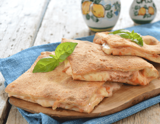 Pizza coperta on a wooden board, topped with fresh basil leaves and served on a blue cloth.