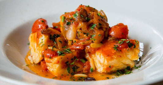 Baccalà in umido alla Calabrese with tomatoes and herbs on a white plate.