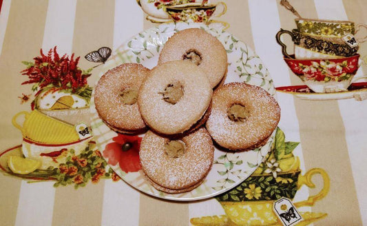 Delicious pistachio occhi di bue cookies dusted with powdered sugar on a decorative plate.