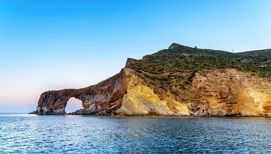 Scenic view of a rocky coastline at sunset with a natural arch and calm waters near Salina, Aeolian Islands.