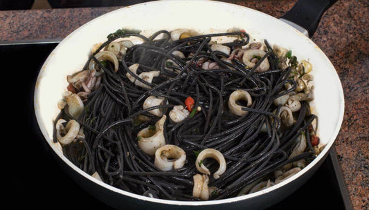 Spaghetti col nero di seppia cooking in a pan with squid and herbs.