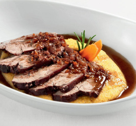 Sliced tender beef served on polenta with rich sauce and garnished with carrots.