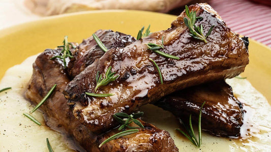 Delicious Tuscan pork ribs garnished with fresh rosemary, served on a yellow plate.