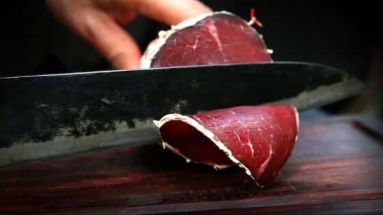 Salame di Capra being sliced with a knife, showcasing its rich red color and texture.
