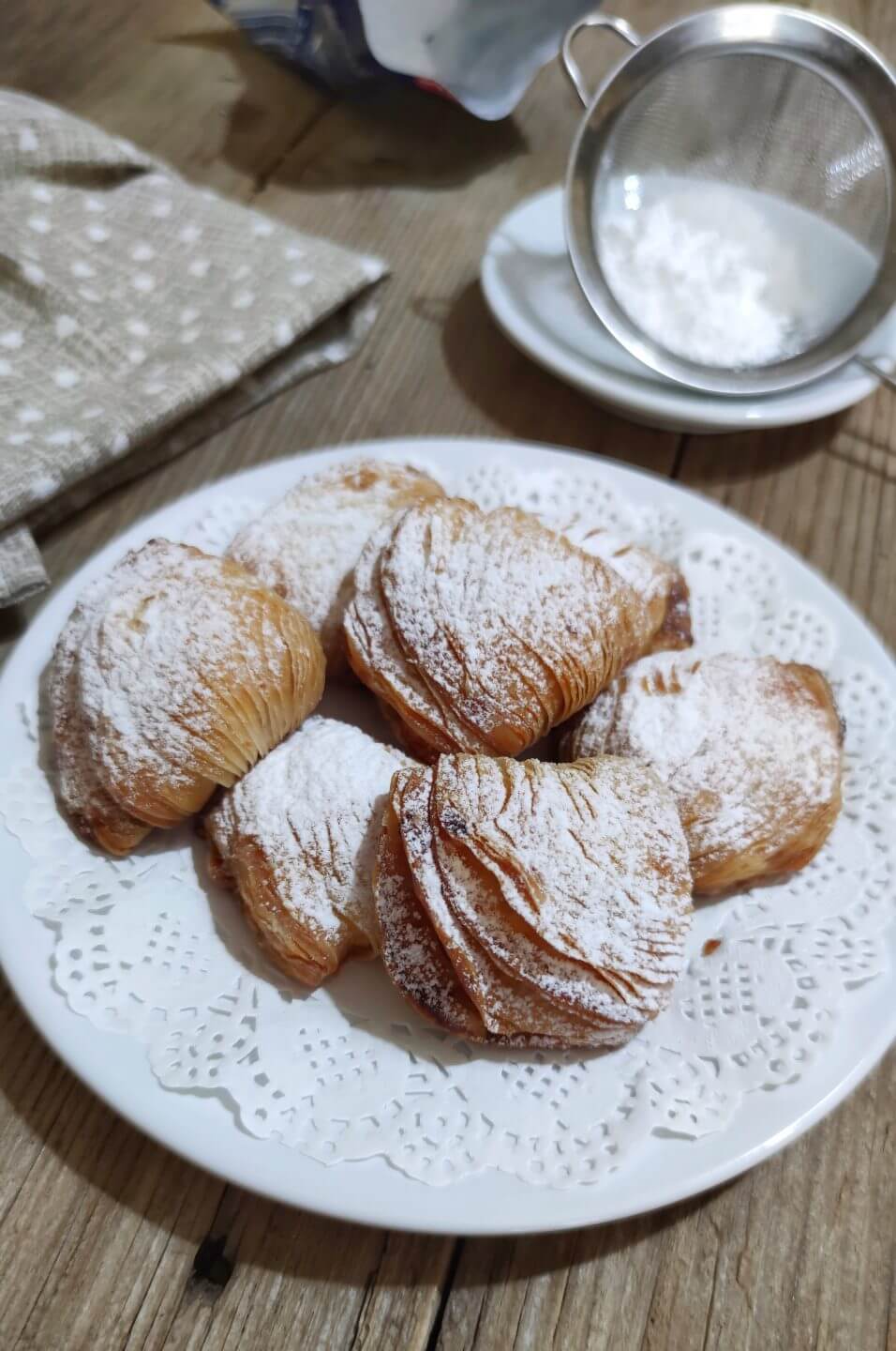 Sfogliatella Riccia on a lace plate, dusted with powdered sugar, showcasing their flaky texture and artisanal quality.