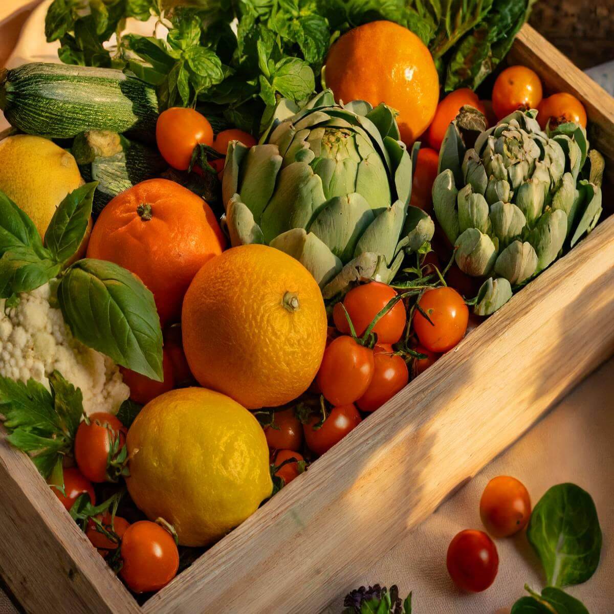 Cassetta di agrumi e ortaggi freschi di stagione, compresa una varietà di limoni, arance, pomodorini e carciofi.