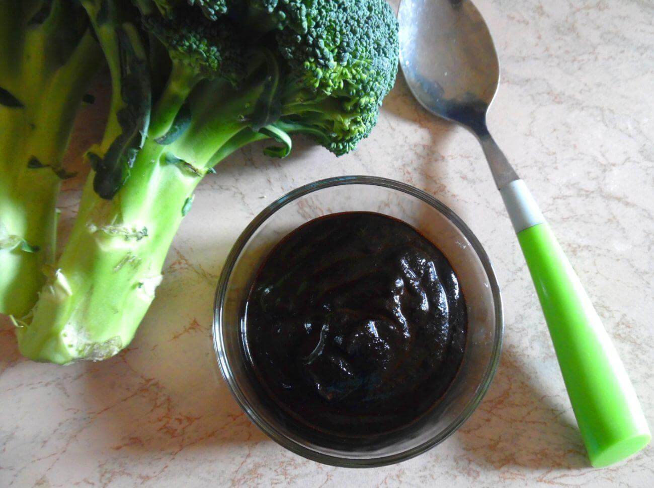 Bowl of nero di seppia on a countertop with fresh broccoli and a spoon, ideal for seasoning dishes.