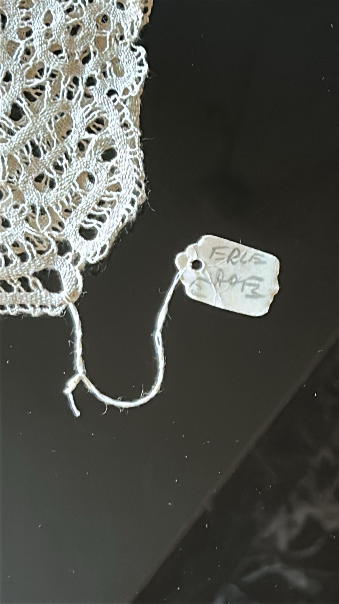 Close-up of intricate Burano lace with a tag reading 'FRL 248' on a dark surface.