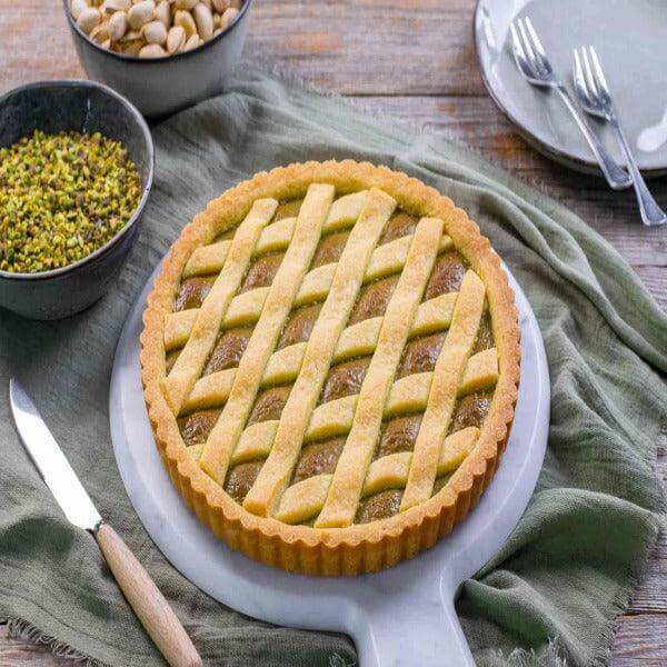 Crostata artigianale al pistacchio con frolla dorata, accompagnata da pistacchi e mandorle.