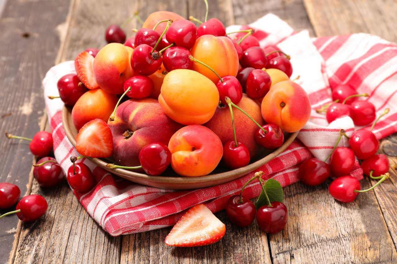 Mixed seasonal fruit bowl featuring cherries, apricots, and peaches on a rustic wooden table.