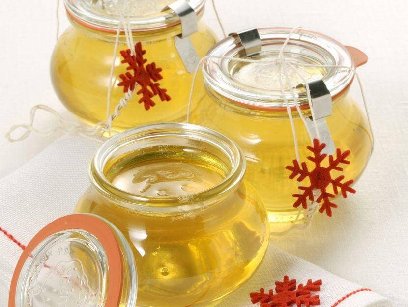 Three glass jars filled with golden liquid, adorned with red snowflake decorations, set on a linen napkin.
