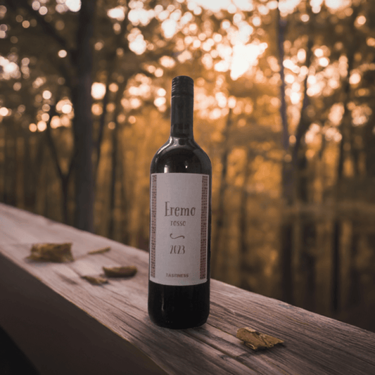 Bottle of Vino Rosso Eremo 2023 on a wooden table in a sunlit forest setting.