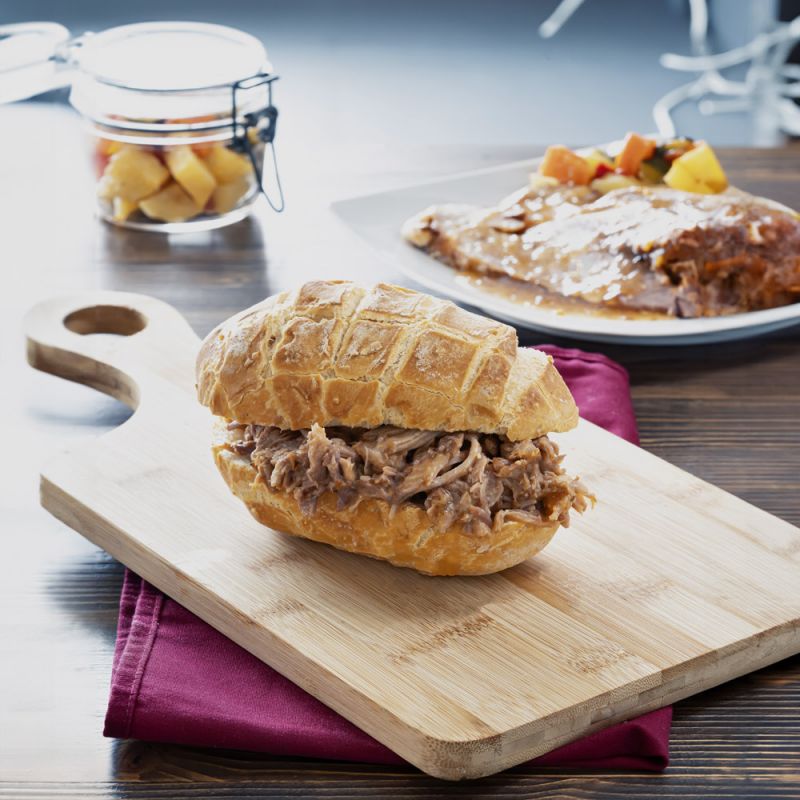 Pulled Porck in a sandwich on a wooden board, showcasing tender and flavorful meat.