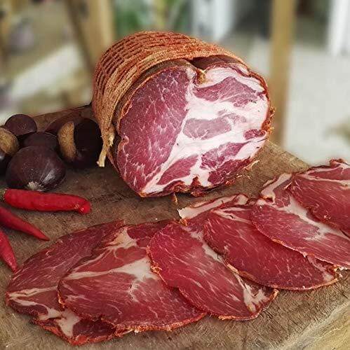 Capocollo legato a mano affumicato e stagionato, servito su un tagliere con peperoncini e frutta.