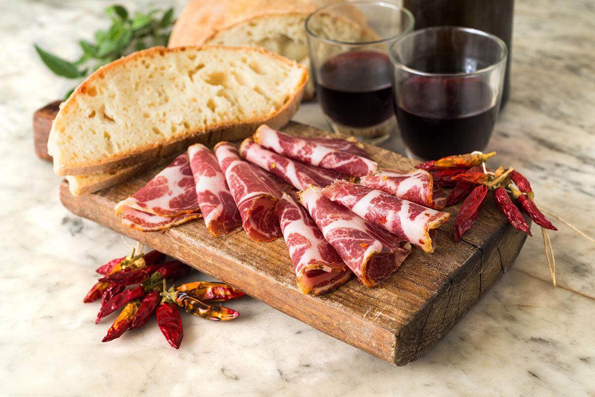 Delicious Capocollo legato a mano with bread, red wine, and chilies, showcasing Calabria's prized salumi.